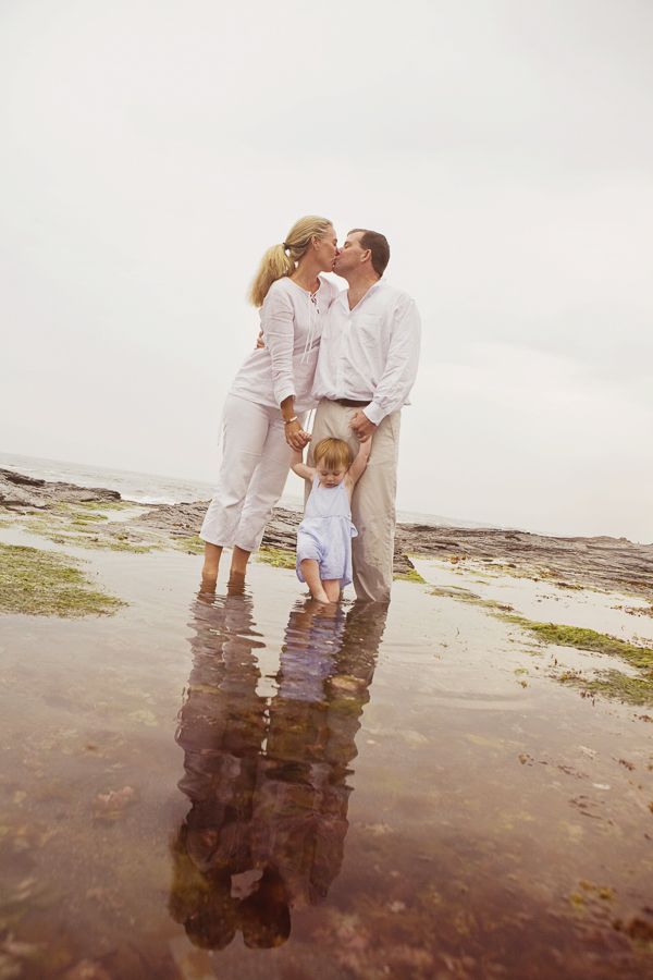Family standing in shallow water at beach with reflections at sunset.