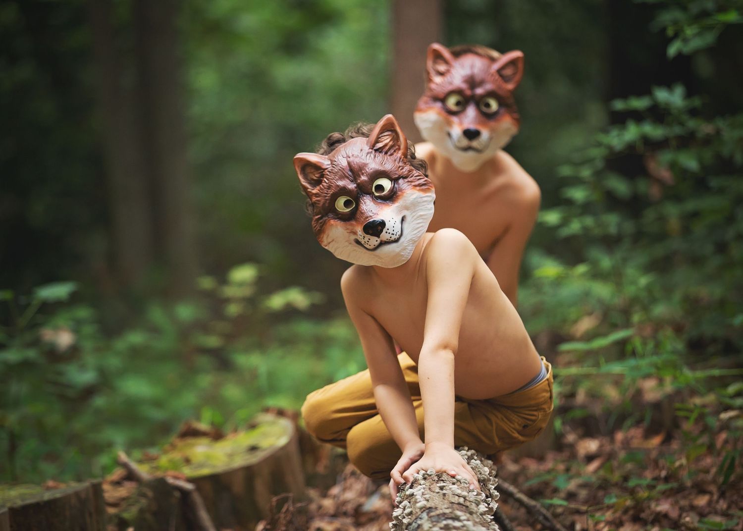 Two fox-masked figures playing in the woods wearing whimsical costumes.