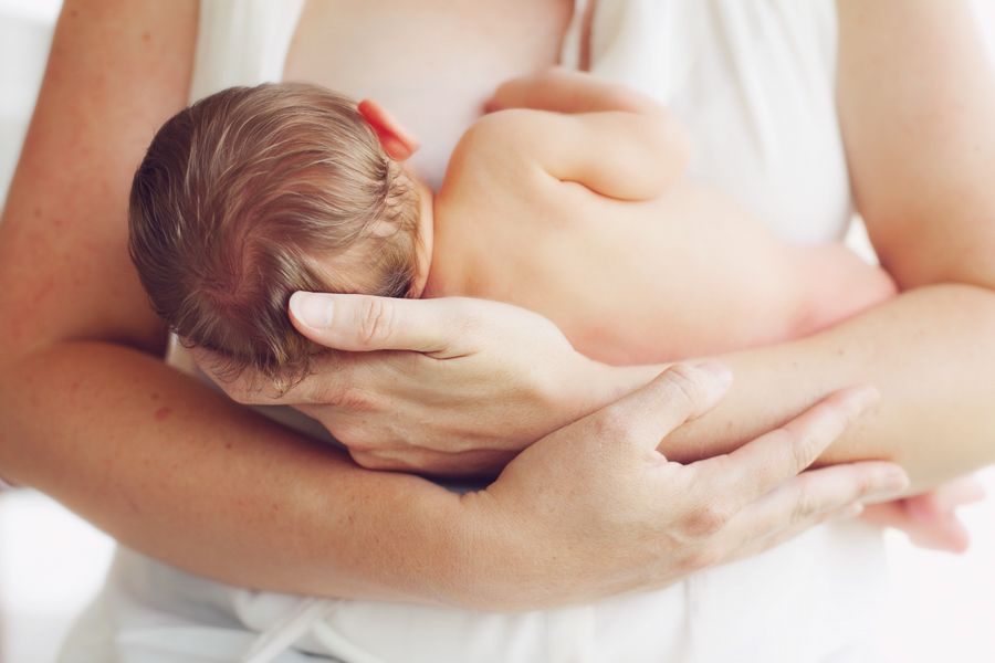 Mother cradling newborn baby tenderly against white background.