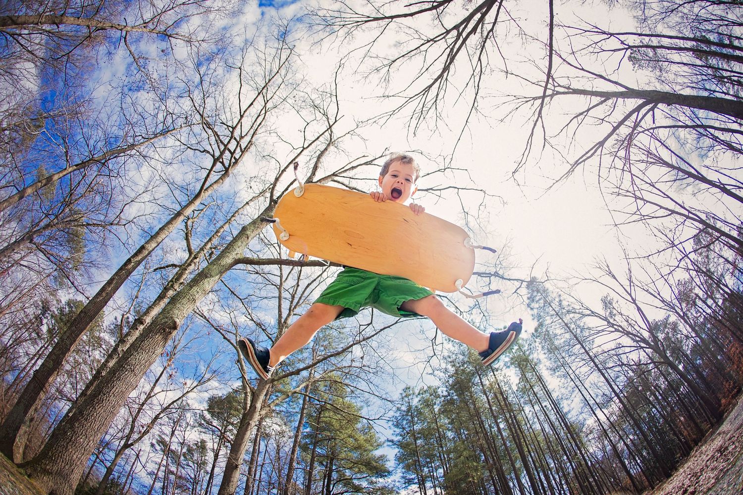Person jumping high against a winter sky with leafless trees below.