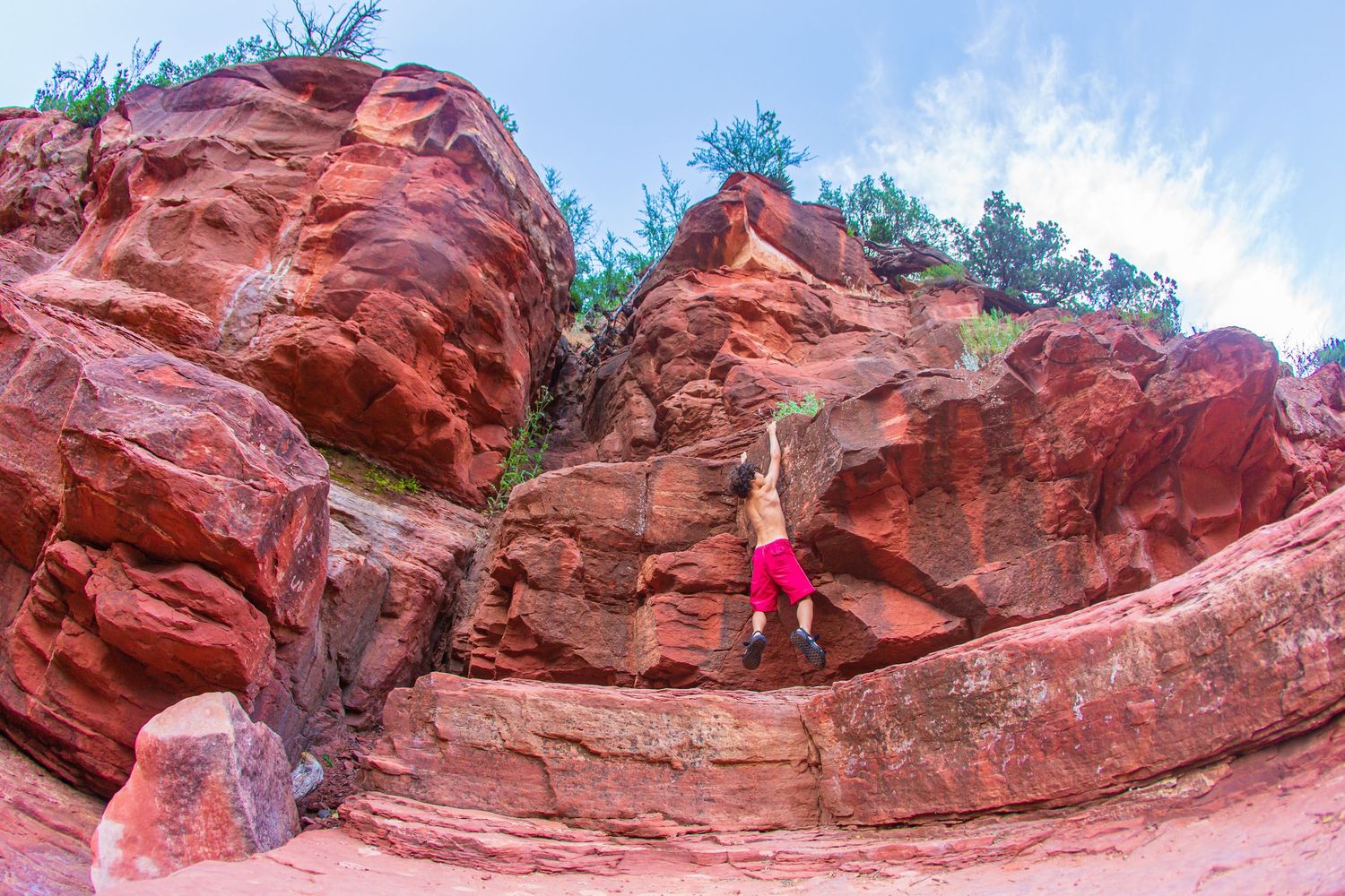 Rock climber scaling a red sandstone cliff face against blue sky.