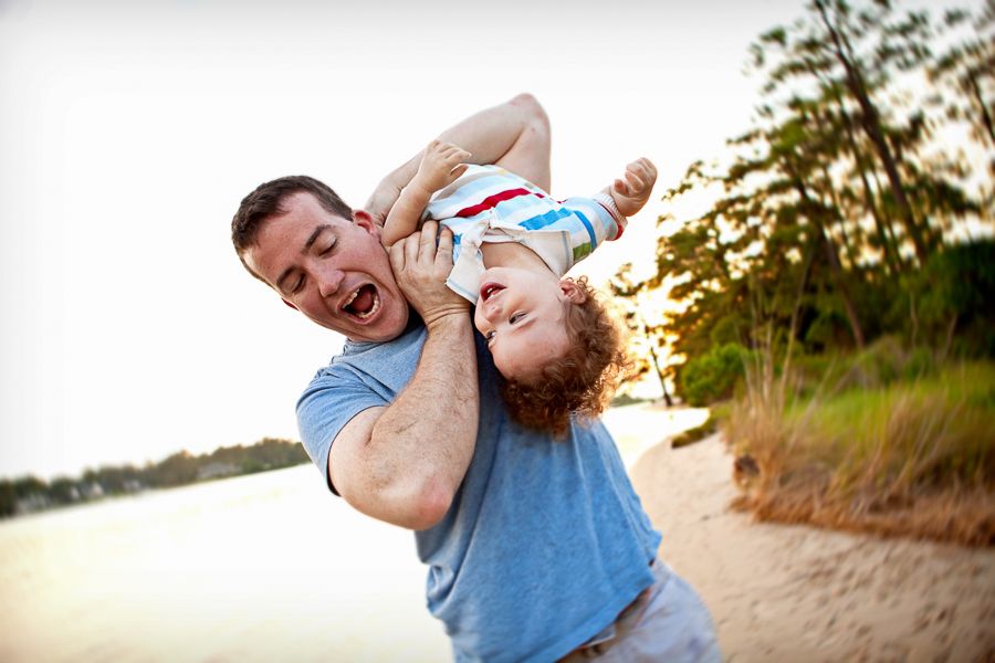 Playful moment between parent and child playing upside down at beach during sunset.