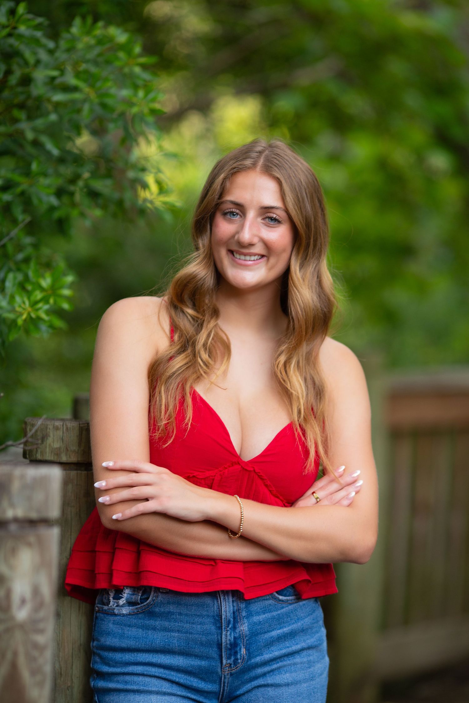 A woman in a red top poses outdoors against a blurred green garden background.