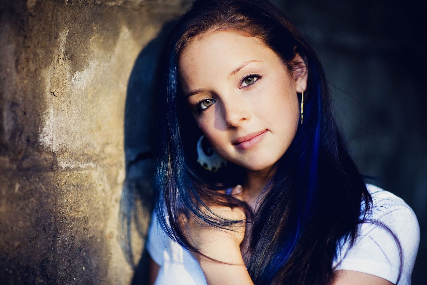 Artistic portrait against textured wall with dramatic lighting.