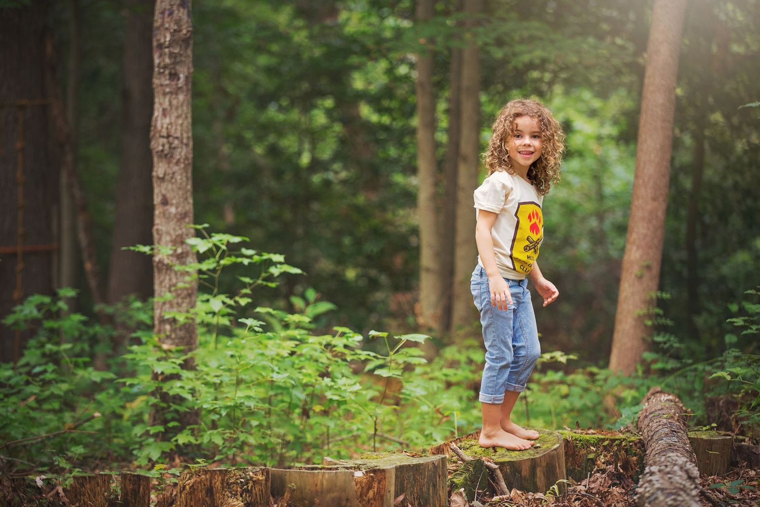 A figure stands on a fallen log in a lush green forest.