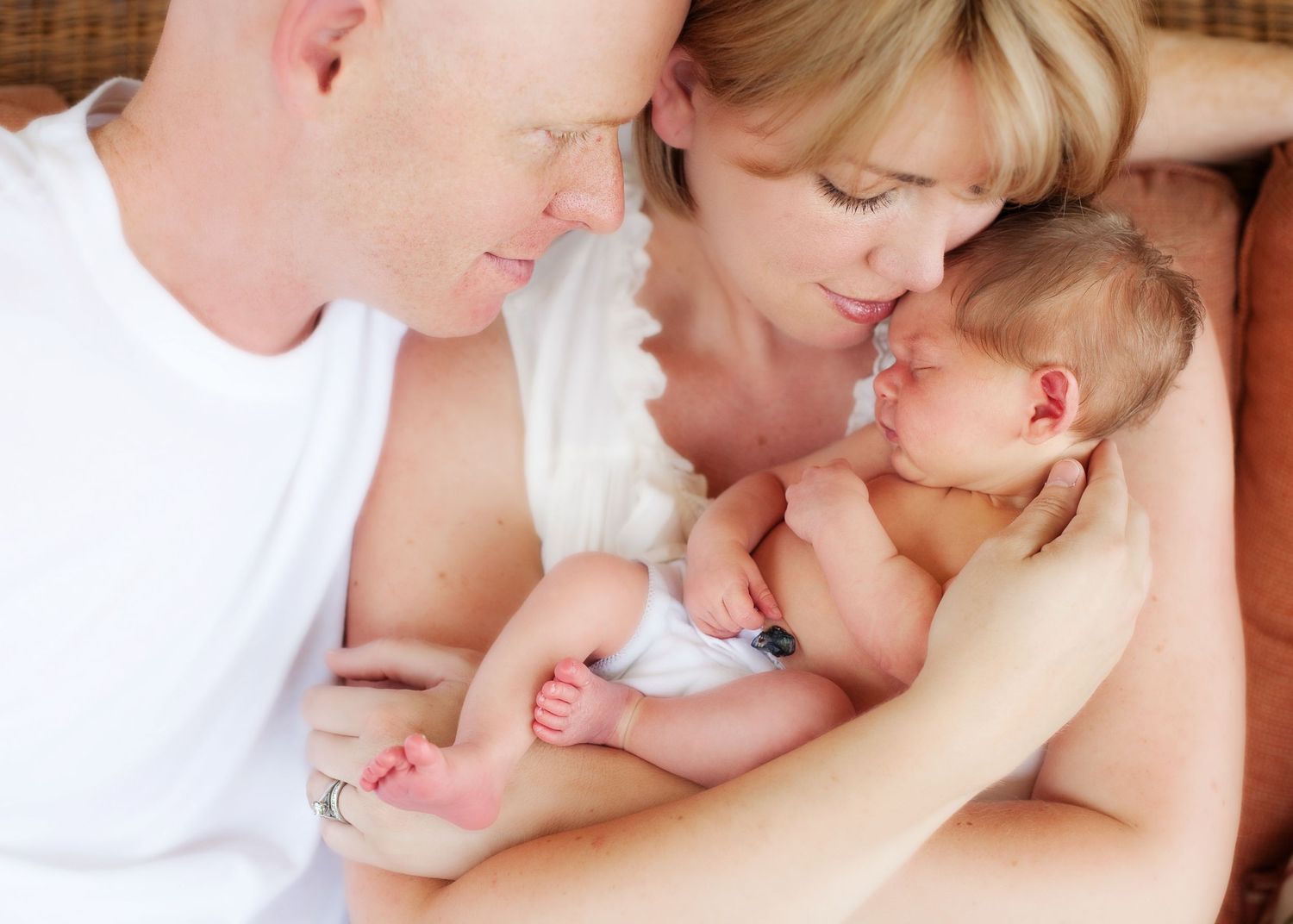 Parents sharing intimate moment with newborn baby on soft bedding.