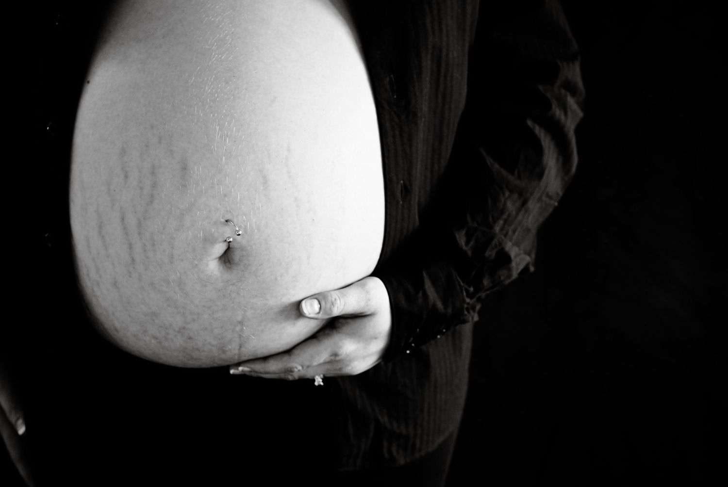 A black and white close-up photograph of a pregnant belly with hands gently cradling it.