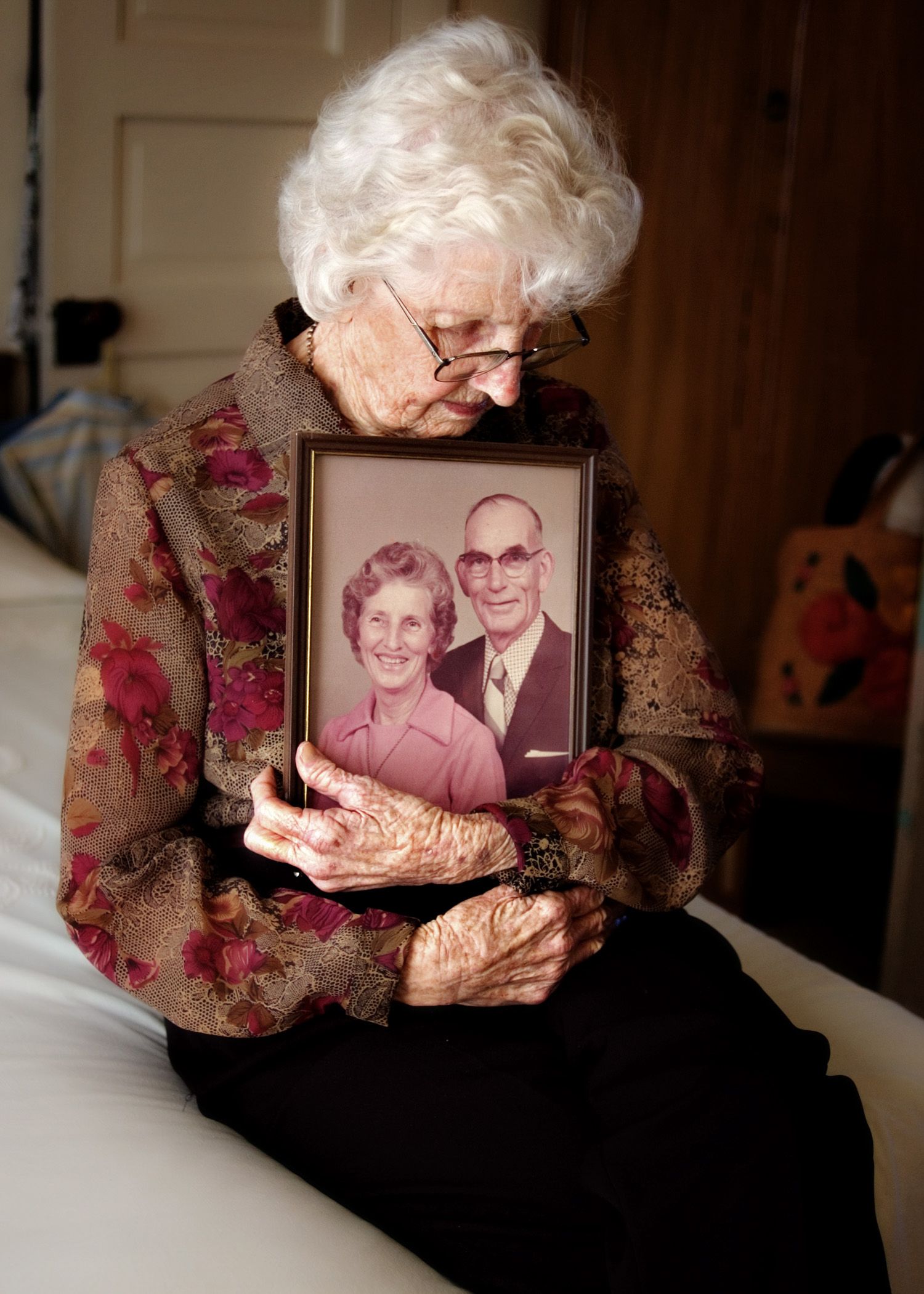 Elderly person holding framed vintage photograph in floral dress.
