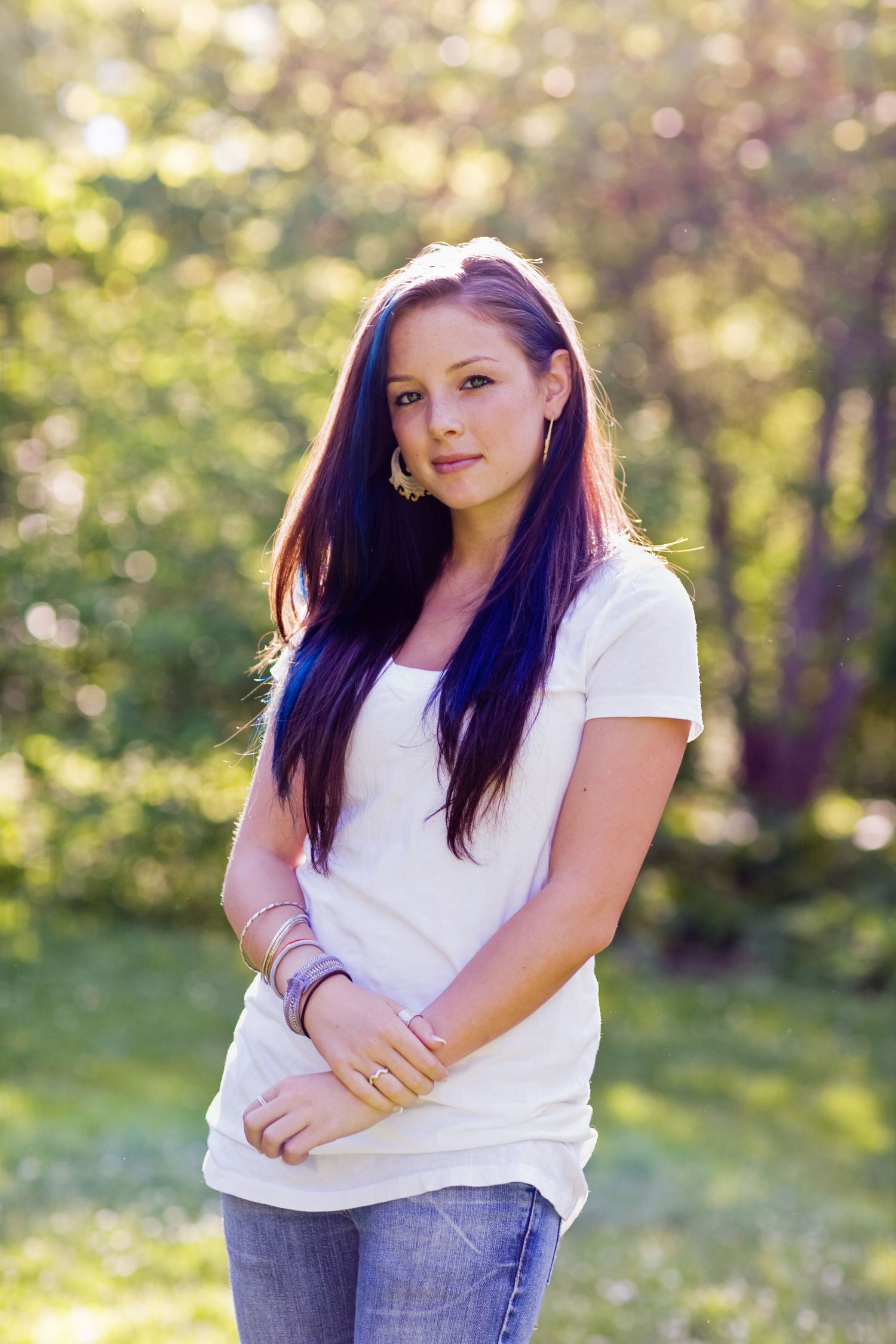 Casual outdoor portrait with purple hair and white t-shirt against blurred nature background.