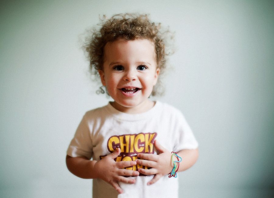 Happy toddler in white t-shirt smiling against light background.