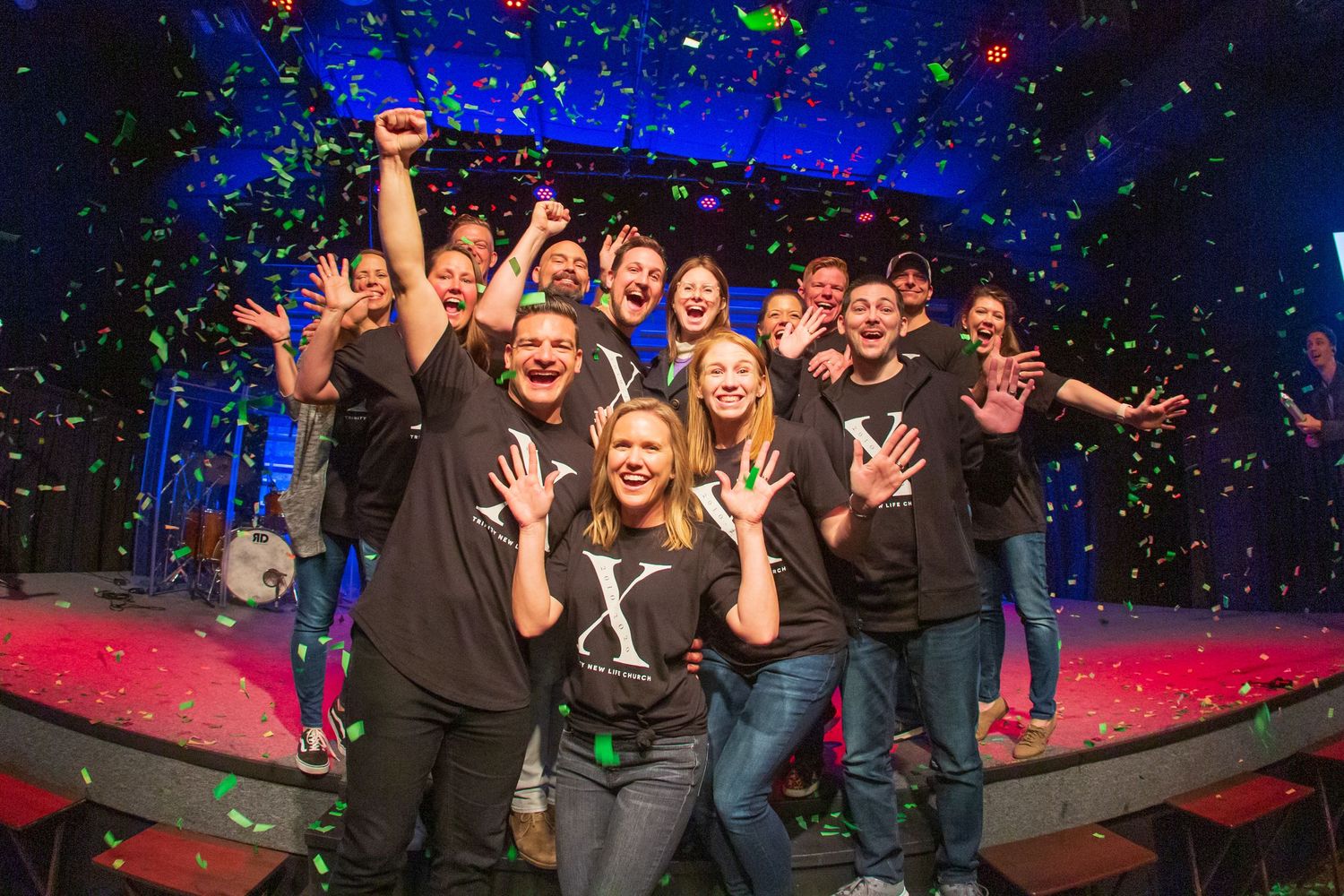 Group of performers celebrating on stage with colorful confetti falling.
