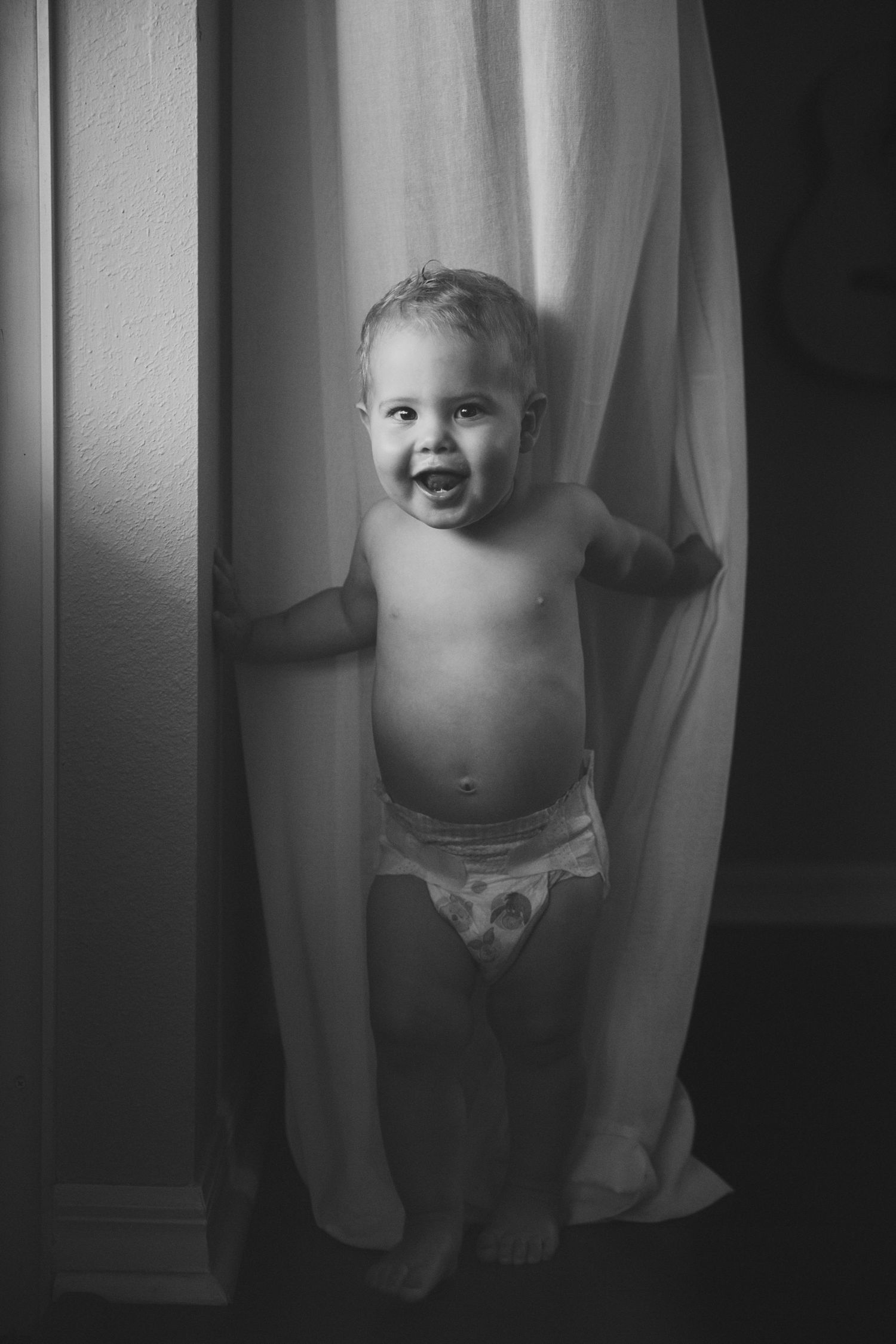 Joyful moment captured as small figure plays peek-a-boo with white curtains.
