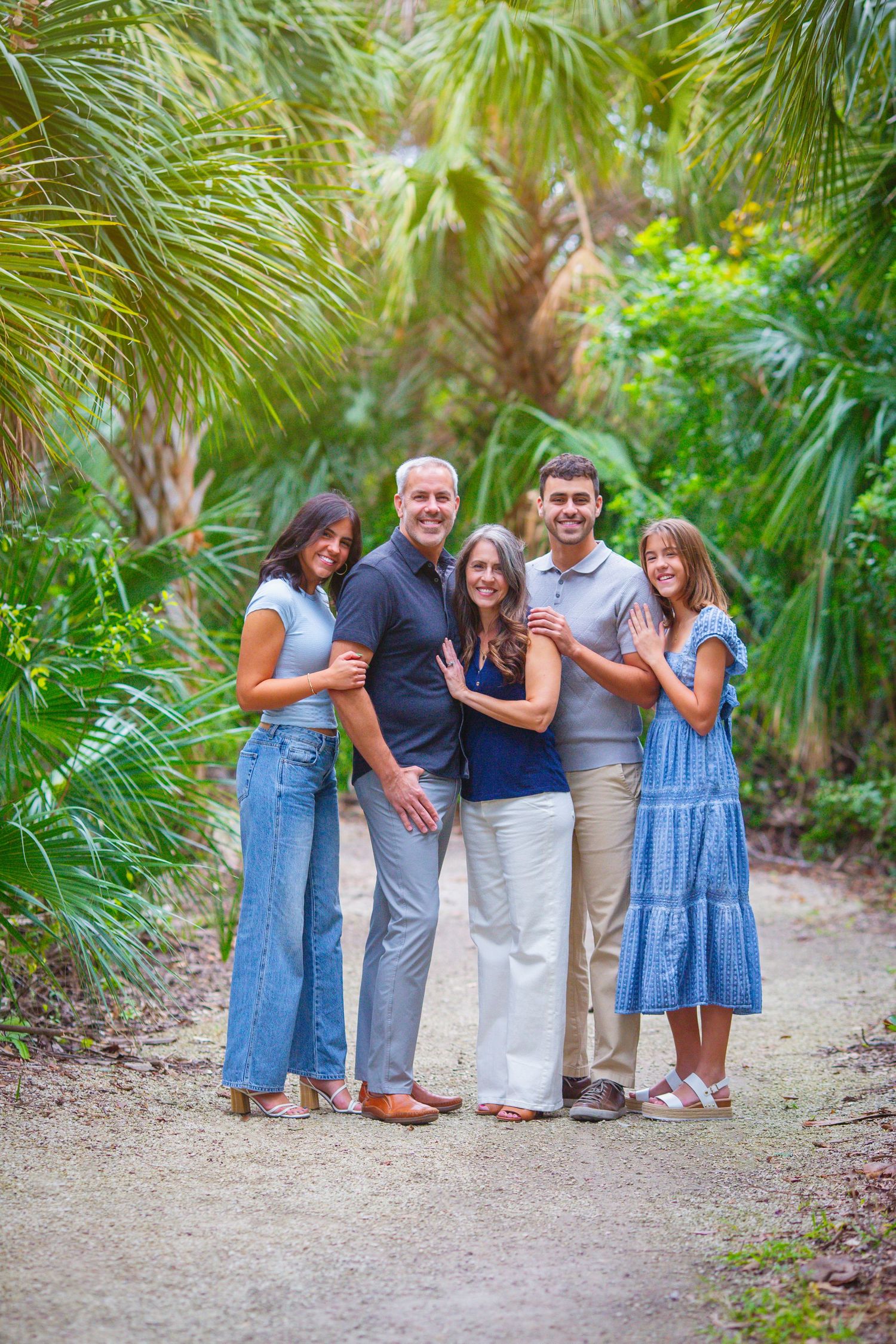 A happy family group poses together on a path surrounded by tropical palm trees.