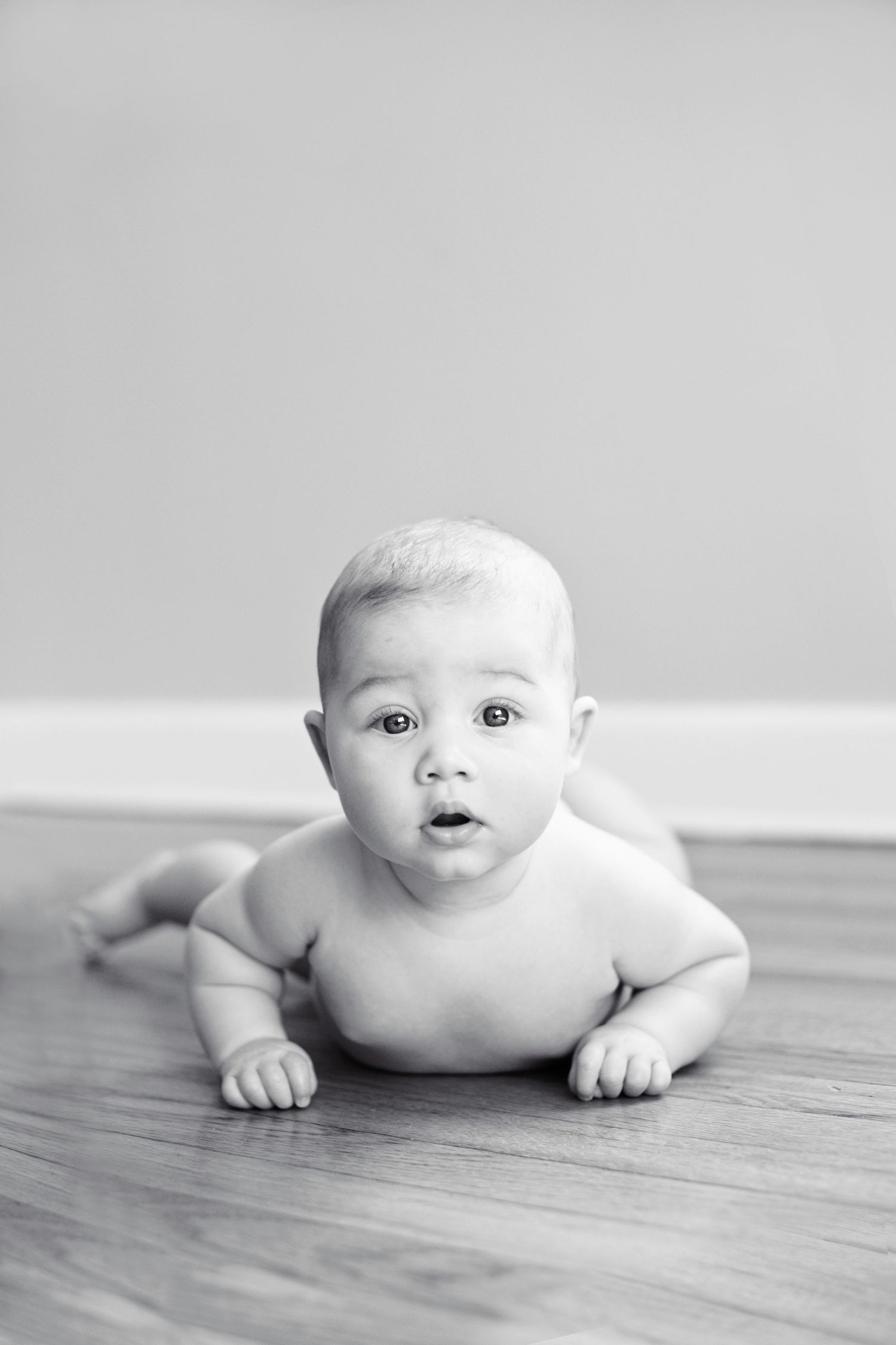 A curious baby lying on hardwood floor in black and white photography.