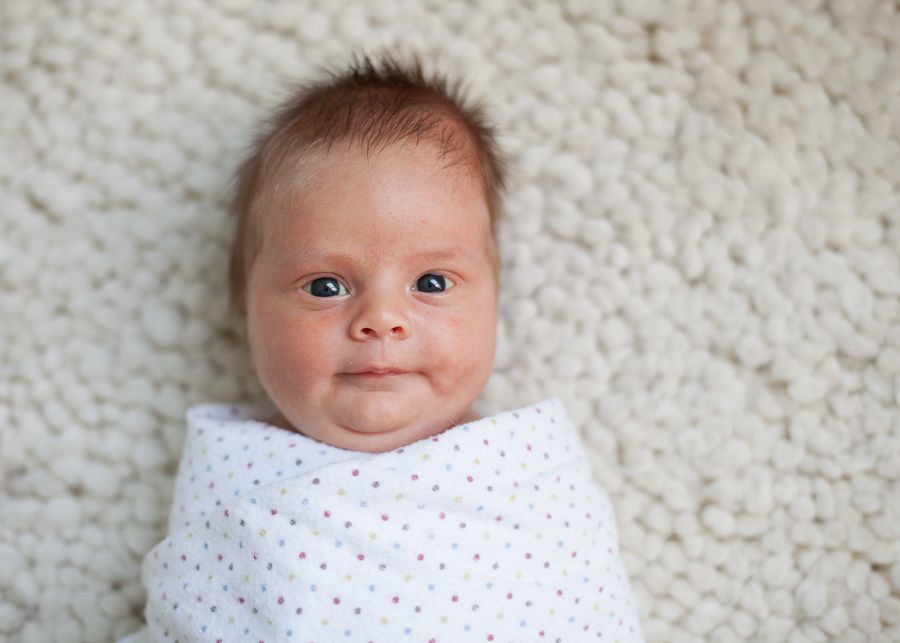 Close up of adorable baby in white polka dot swaddle against textured carpet.