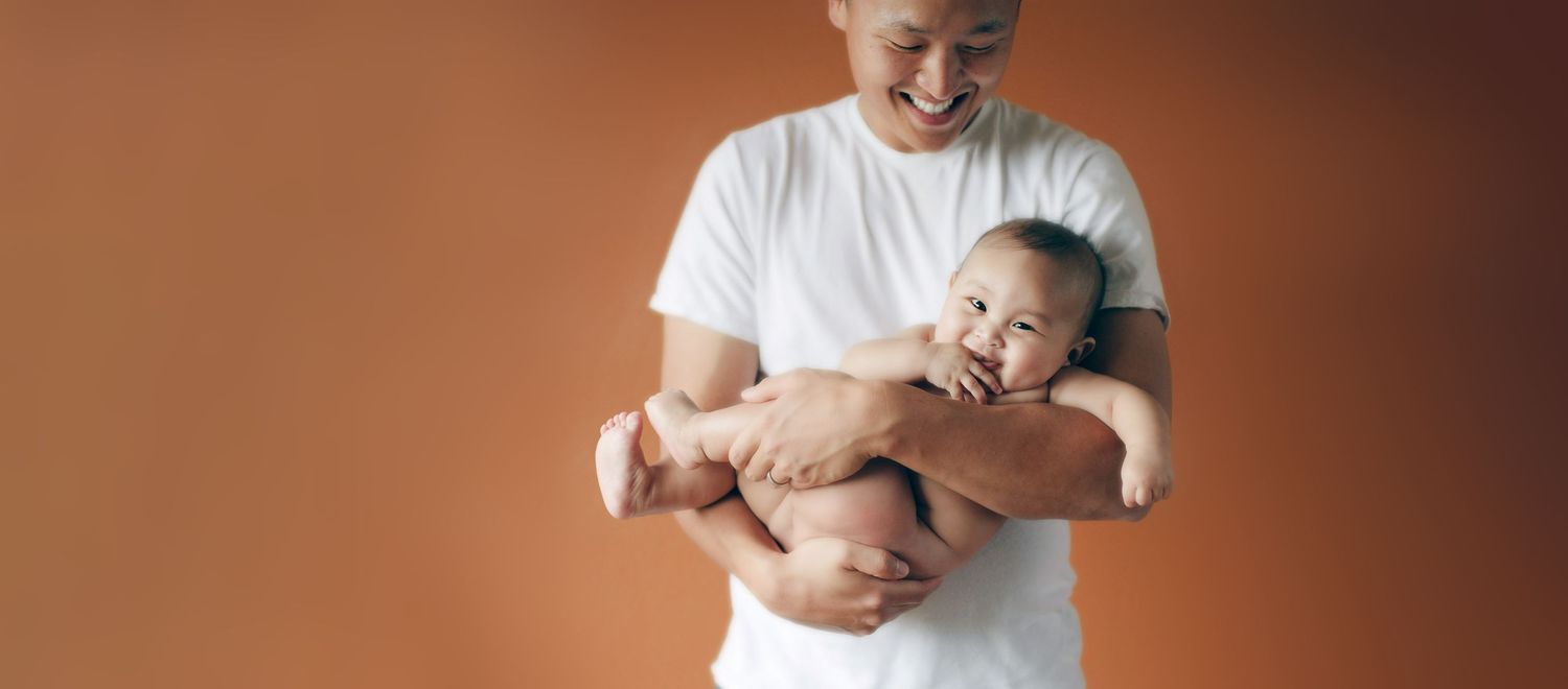 A person in white shirt holding and playing with happy baby against orange background.