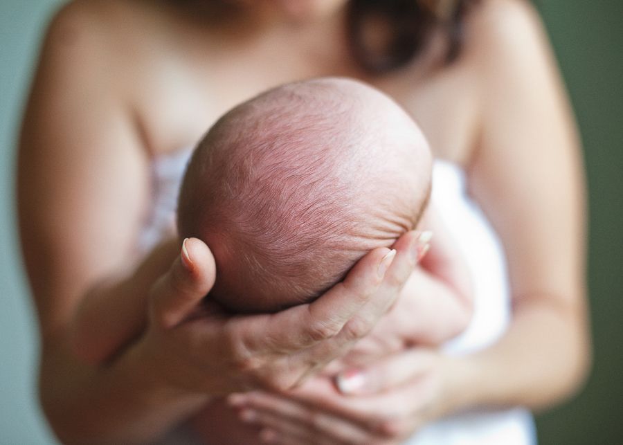 A newborn baby being cradled gently in hands against a soft green background.