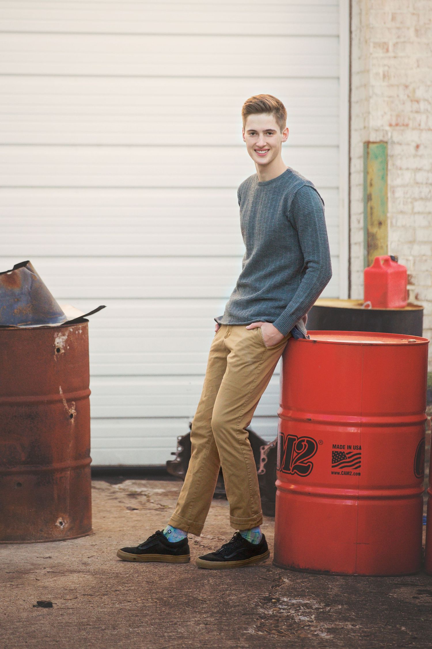 Casual portrait of someone in a gray sweater and khakis standing between red industrial barrels.
