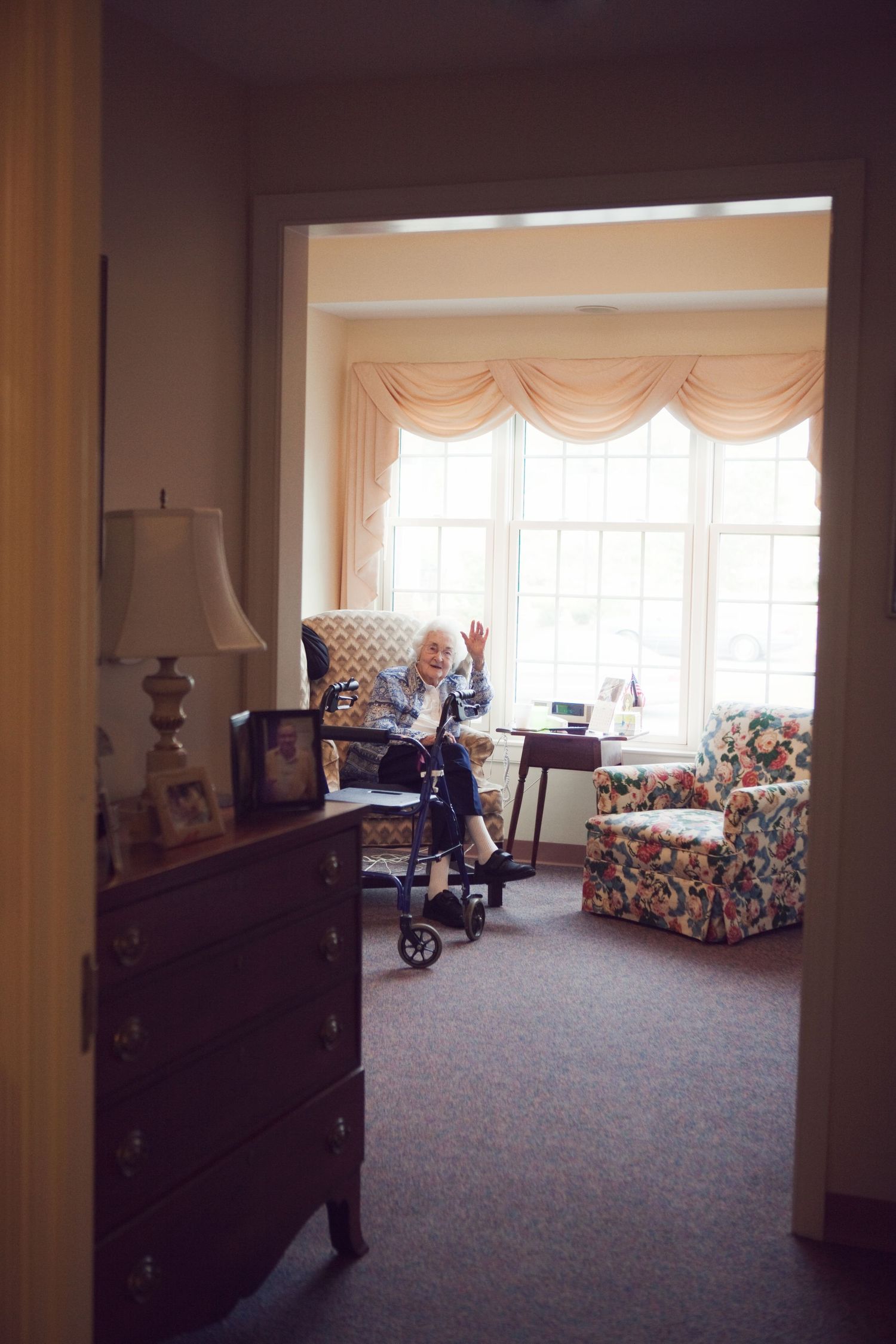 A view through a doorway shows a sunny room with floral furniture and window treatments.