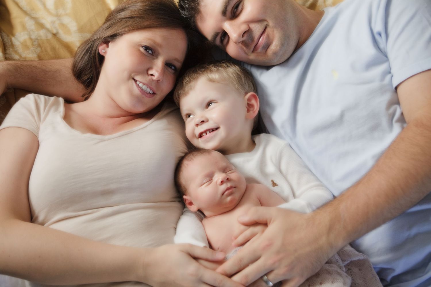 Joyful family moment with newborn baby and young child on cozy bed.