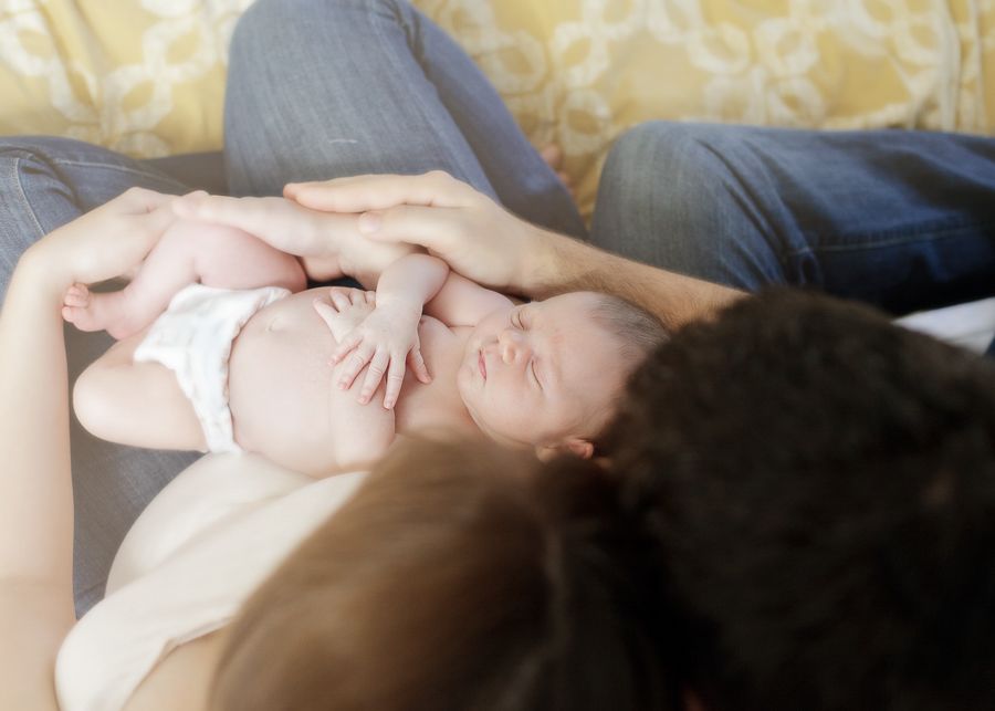Tender moment as parents cuddle with their newborn baby on a bed with yellow pillows in the background.