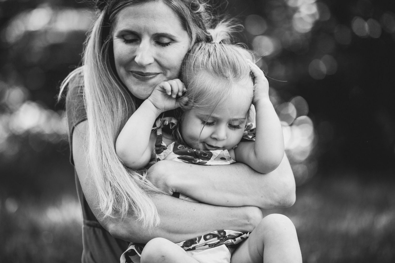 Black and white portrait capturing tender embrace outdoors with bokeh background.