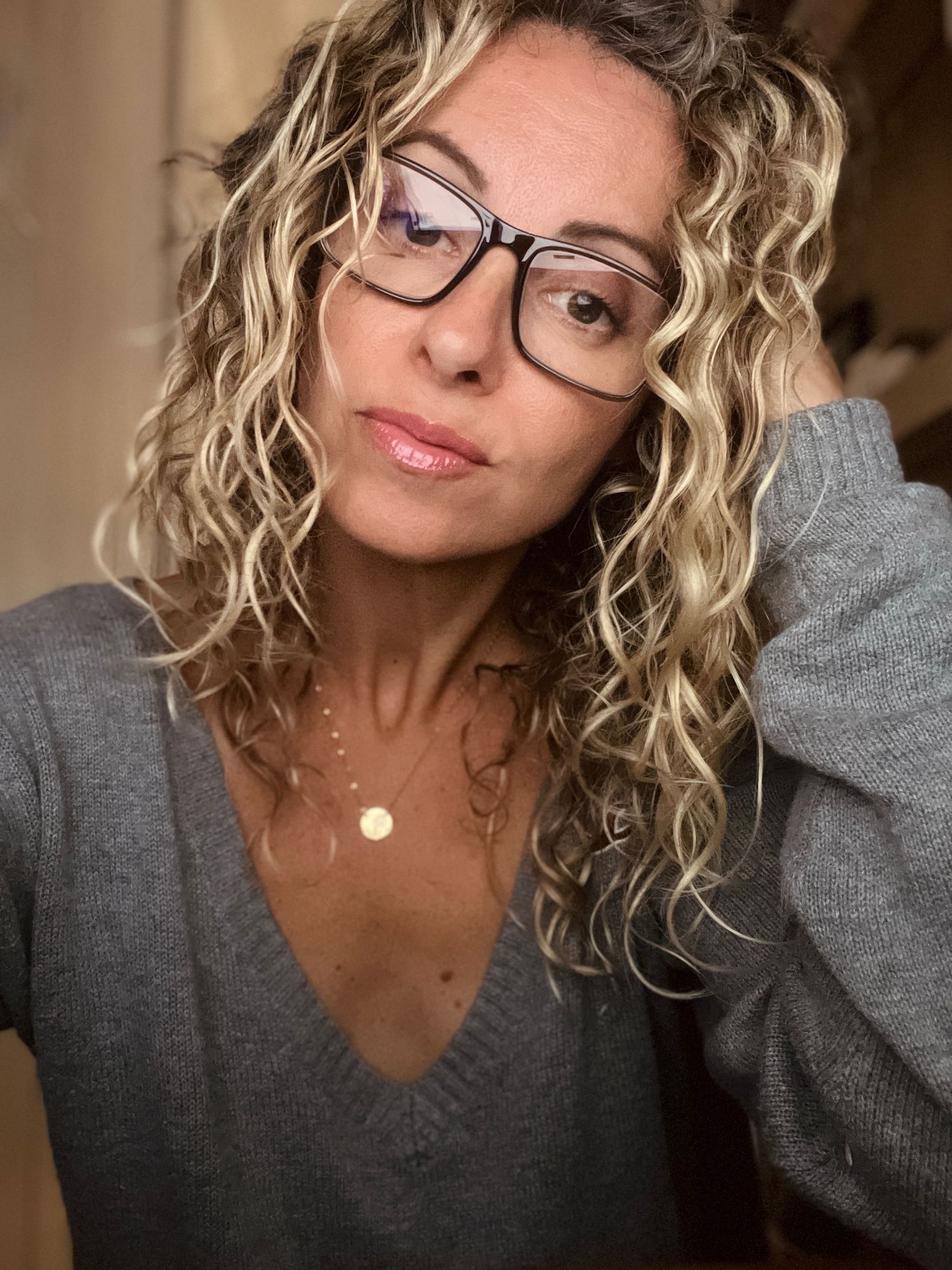 Self portrait of person with curly blonde hair wearing glasses and gray sweater.