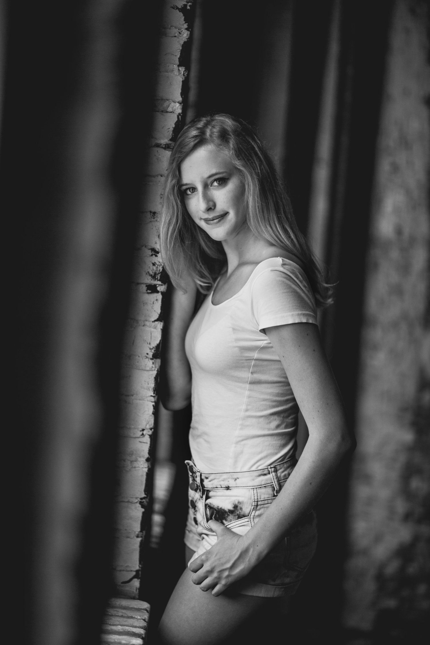 Black and white portrait of someone leaning against a birch tree in casual attire.