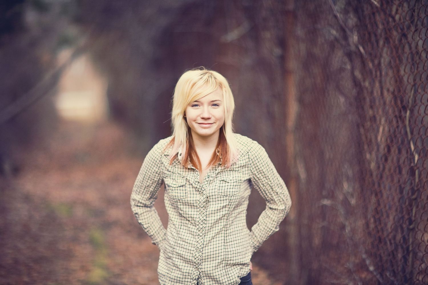 Portrait of a person in a checkered shirt standing outdoors with a dreamy blurred forest background.