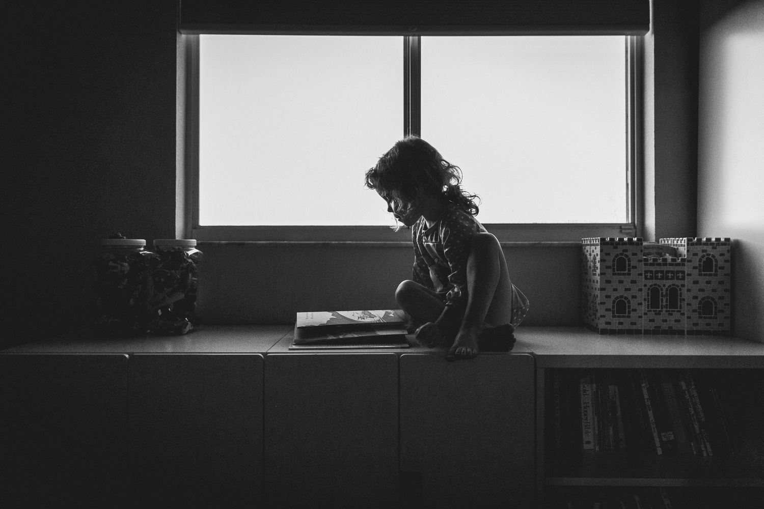 Black and white silhouette reading by window with natural light streaming in.