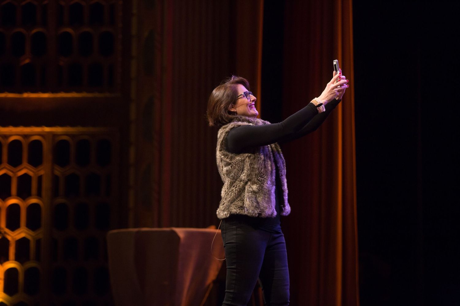 Performer gesturing dramatically on stage with orange backdrop lighting.