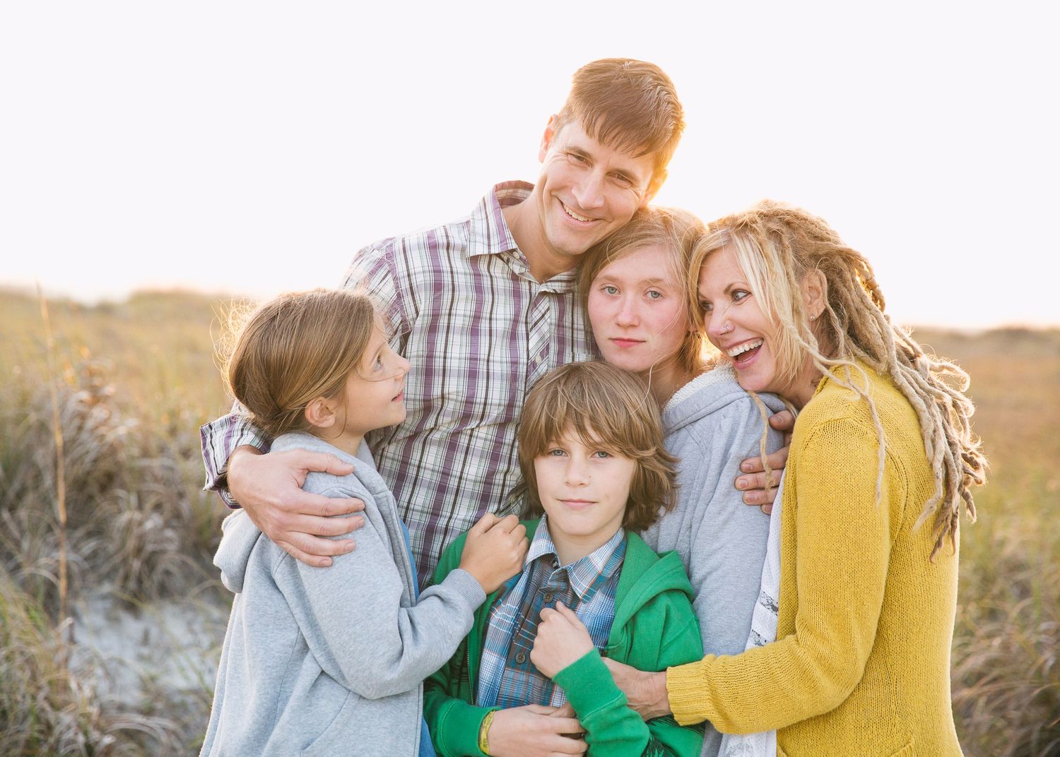 Family group poses together outdoors at sunset in casual clothing.