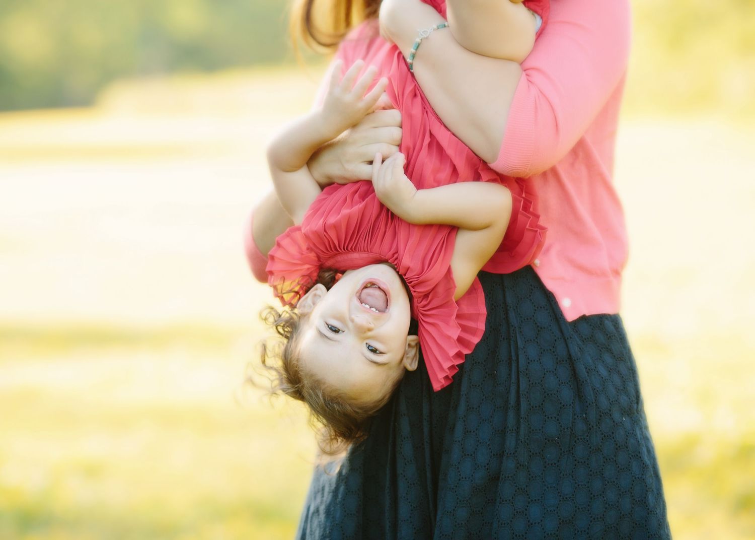 Joyful moment of parent holding child upside down while playing outdoors in pink clothing.