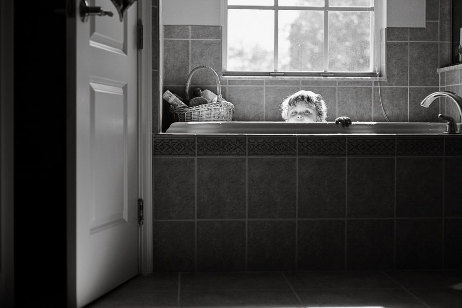 Black and white photo of a bathtub with toys visible through an open doorway.
