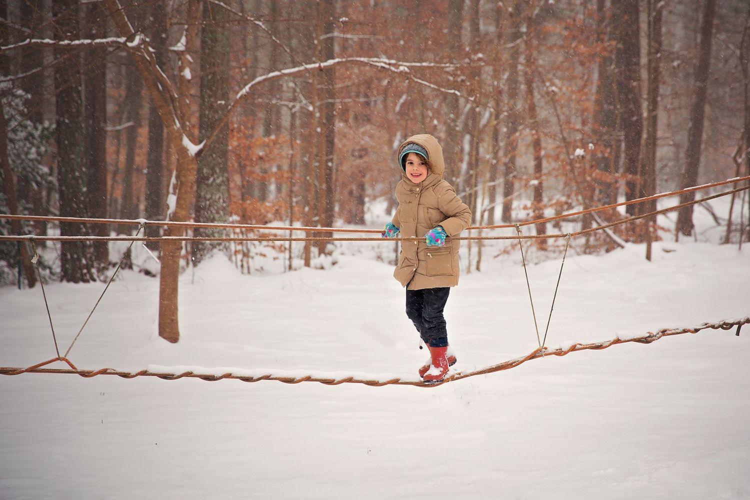 Person in yellow coat walking on slackline in snowy winter forest.