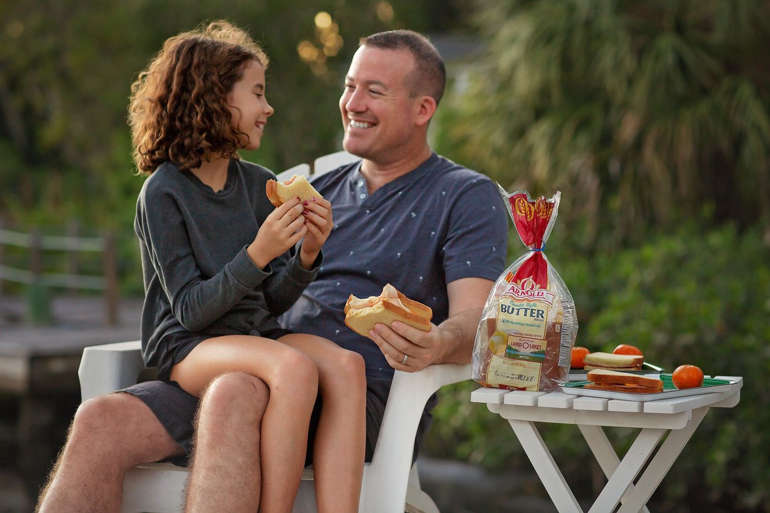 Two people sharing sandwiches and snacks outdoors during a casual picnic.