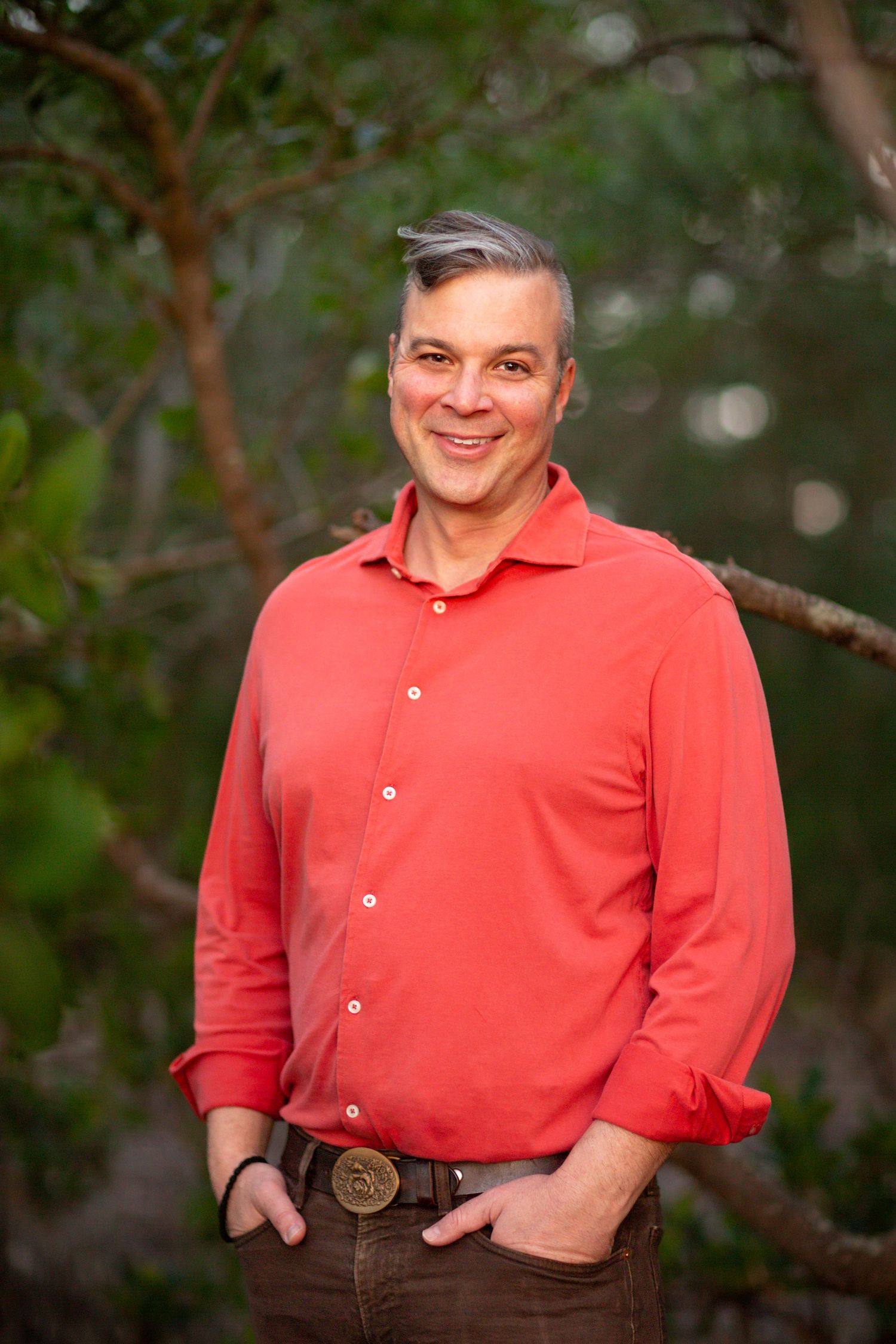 Professional outdoor portrait of person in coral button-down shirt against natural background.
