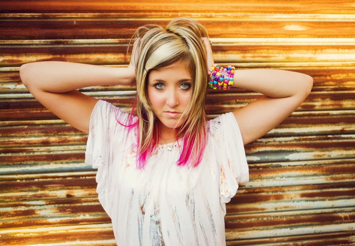Artistic portrait with pink hair highlights against wooden backdrop in warm lighting.