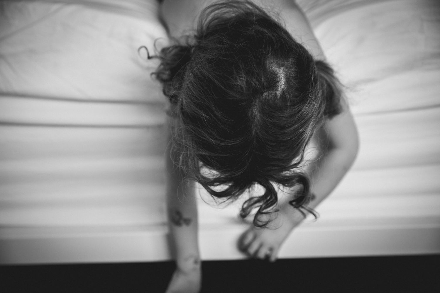 Overhead black and white view of curly hair against white bedding.
