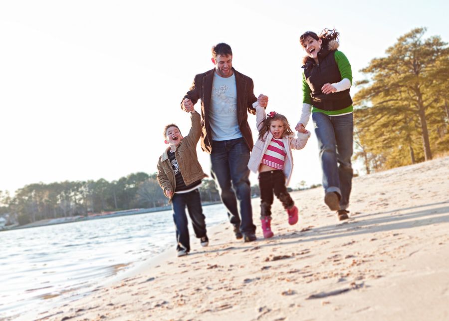 Family running and playing together along beach shoreline at sunset.