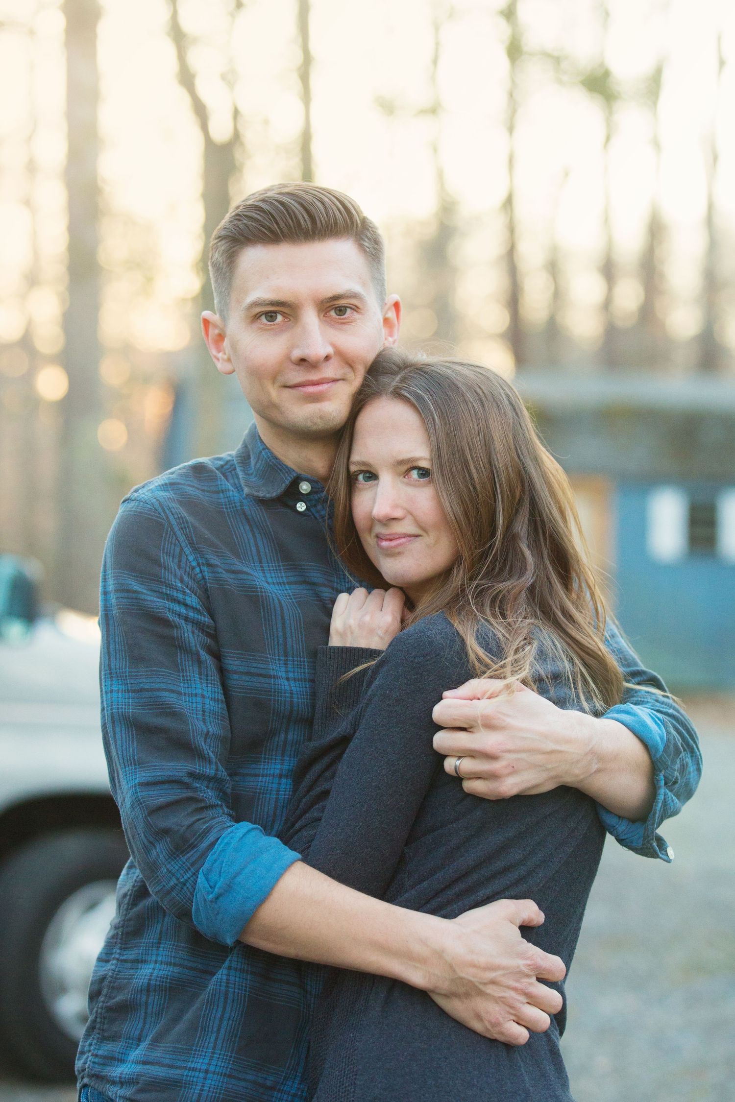 A couple embraces outdoors during golden hour with soft sunlight filtering through trees.