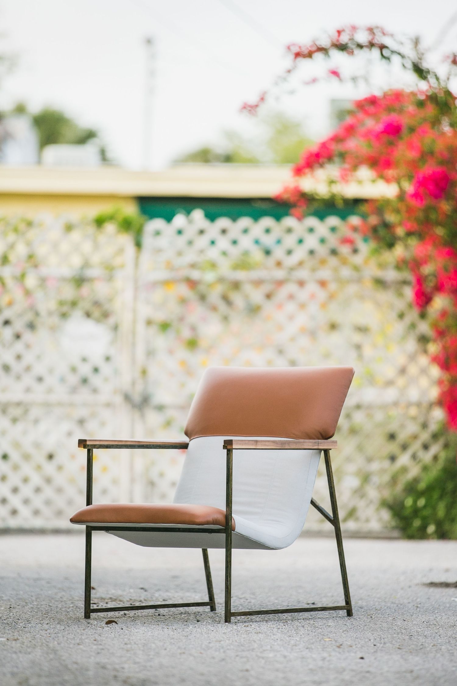 Modern brown chair on concrete patio with flowering bougainvillea in background.