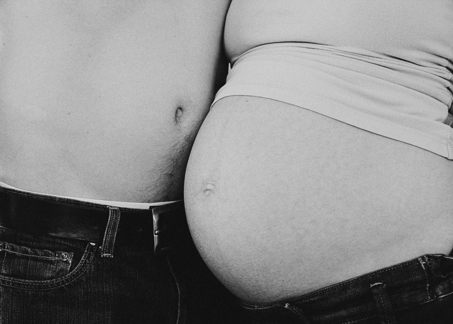 Black and white close-up of two people's torsos showing a pregnant belly.
