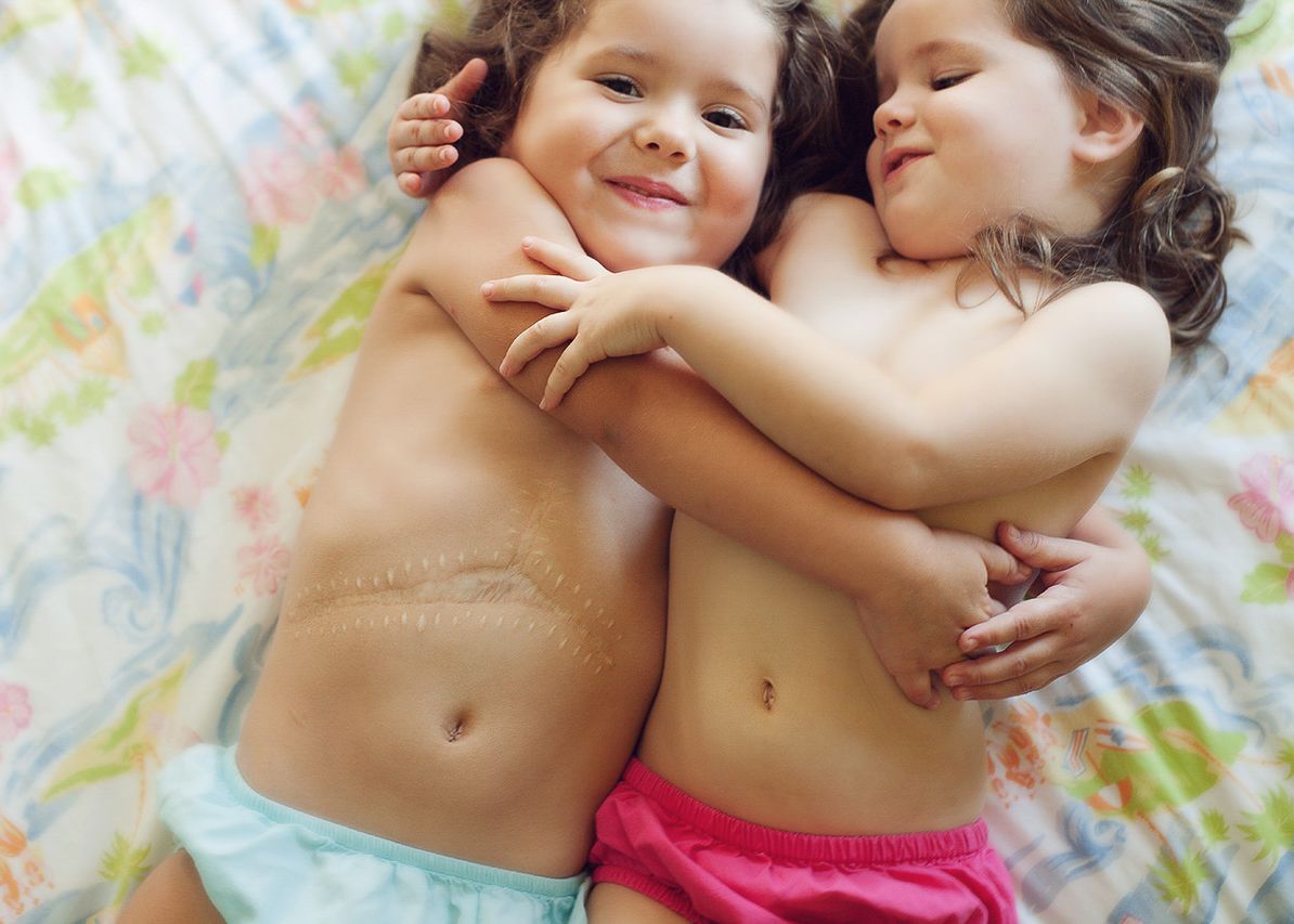 Two young children lying close together on a colorful blanket sharing a joyful moment.