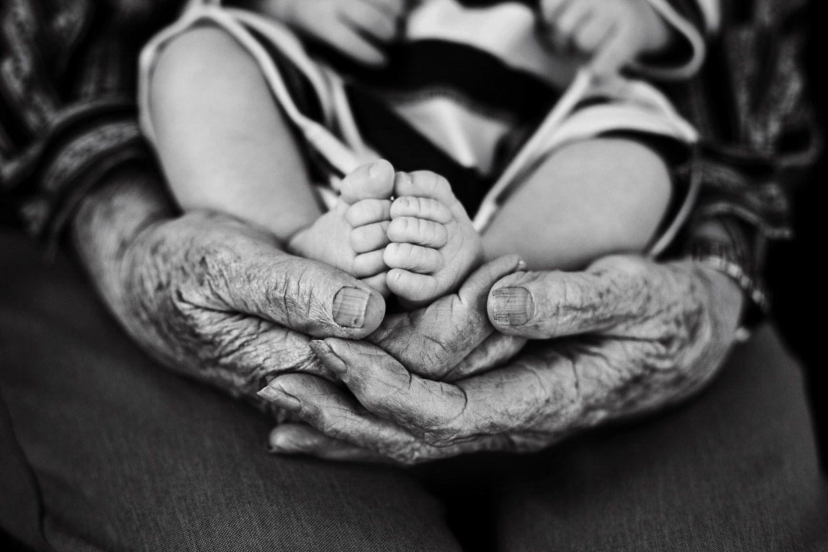 Black and white image showing weathered elderly hands cradling small infant feet.
