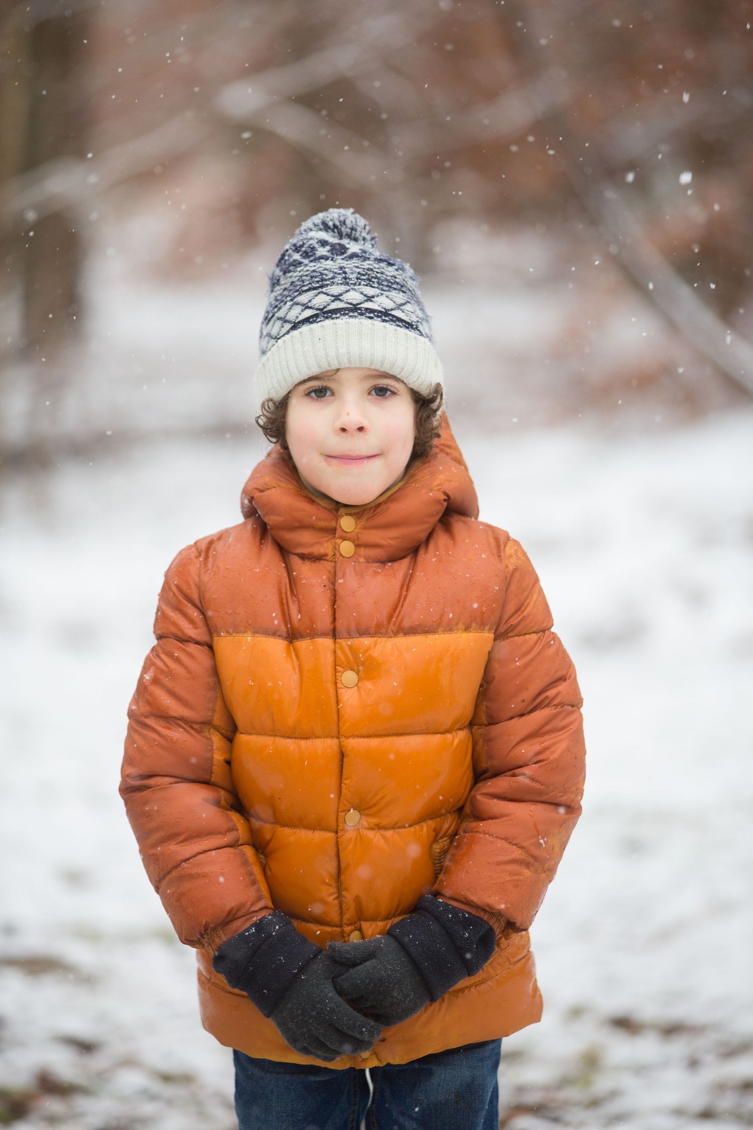Young person bundled up in orange winter coat and knit hat standing in snowy landscape.