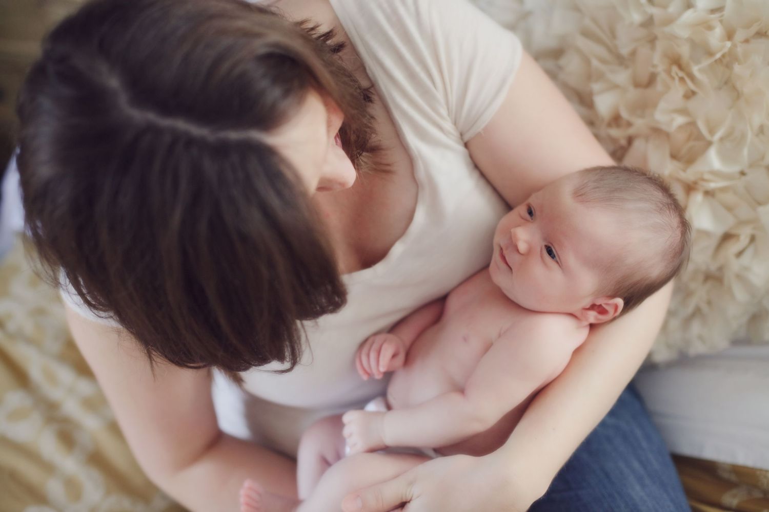 Intimate bonding moment between parent and baby on cream colored bedding.