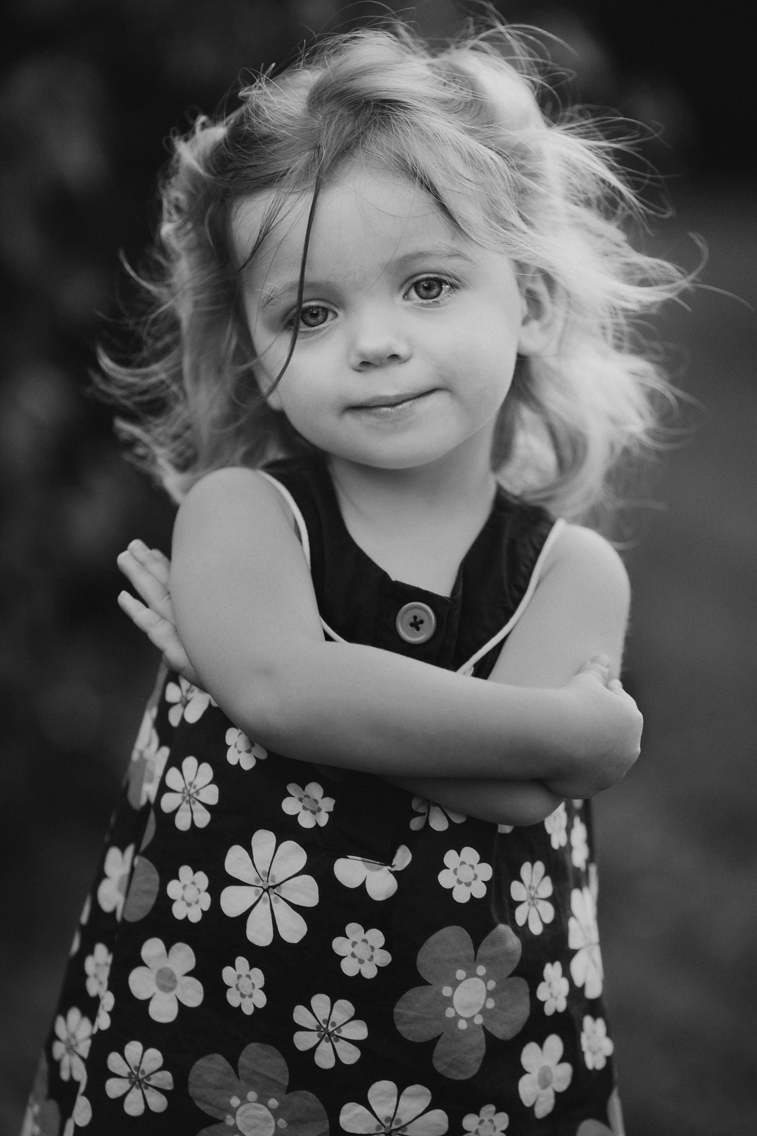 A young child with windswept curly hair wearing a floral dress poses against a dark background.