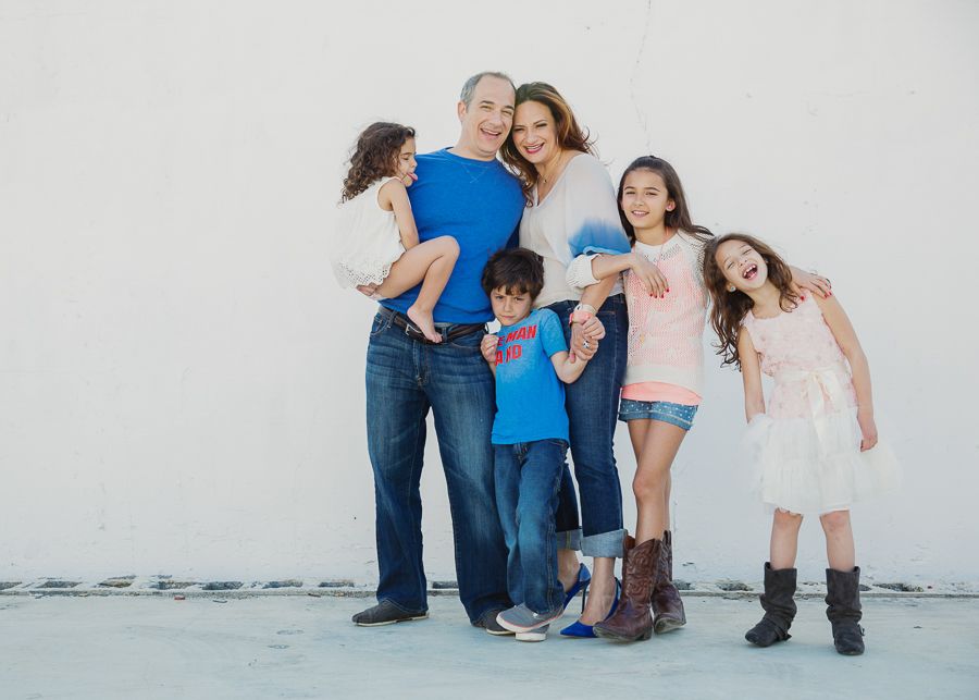 Casual family portrait against white wall showing playful expressions and poses.