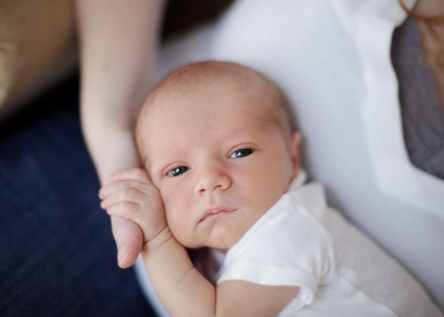 A tiny baby in white clothing gazes at the camera while being held.